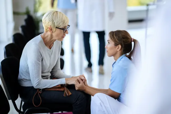 caring-nurse-consoling-mature-woman-waiting-room-medical-clinic